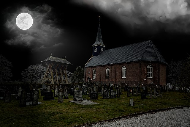 A church and graveyard under a cloudy black sky with a full moon. Spooky Night - Flickr - Alfred Grupstra.jpg Wikicommons
